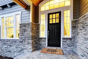 Entranceway to a luxury home that has a double-hung window flanked by casement windows, as well as a front door with an arched window transome and two sidelights