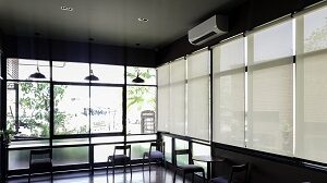 Two walls of windows in a seating area with sheer roller shades pulled down on one wall 